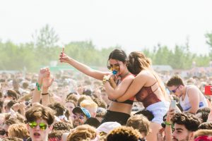 Festival - Two Women Embracing Surrounded by Crowd